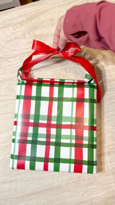 a person holding a wrapped gift bag with a red bow on it's handle