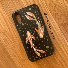 an iphone case with fish painted on it sitting on a wooden floor next to a ruler