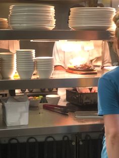 a woman standing in front of stacks of white plates on a counter next to an oven