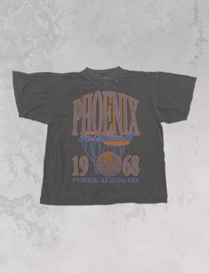 Show the love for your favorite team in this Phoenix, Arizona basketball oversized tshirt that is inspired by vintage 90s N B A tshirts!- Features Phoenix Basketball across the top with a basketball hoop and 1968 with Phoenix, Arizona underneath all in a periwinkle and orange ink- Screen print transfer that is heat pressed onto each tshirt- Tshirt is a super soft vintage wash that gets softer after each wash- Oversized fit- Sizing translation: XS/S = L , S/M = XL , L/XL = 2XL , 2XL/3XL = 3XL - M Retro Oversized Tops For Game Day, Oversized Retro Top For Game Day, 90s Text Print Tops For College, Collegiate Graphic T-shirt For Streetwear, Collegiate Streetwear T-shirt With Graphic Print, Collegiate Graphic Print T-shirt For Streetwear, Sporty Basketball T-shirt With Letter Print, Throwback T-shirt For College Sports Season, Throwback College T-shirt For Sports Season