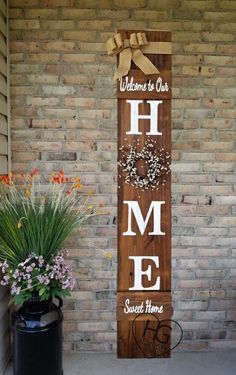 a welcome home sign on the side of a brick building with flowers and potted plants