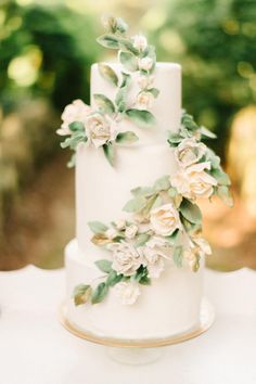 a white wedding cake with flowers and leaves on the top is sitting on a table