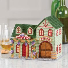 a small house made out of crochet sits on a counter next to wine bottles