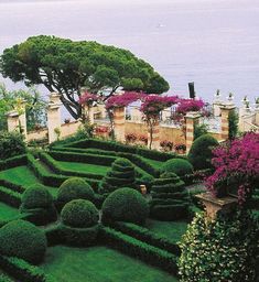 an elaborate garden with hedges and flowers on the side of a cliff overlooking the ocean