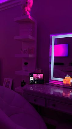 a room with a desk, mirror and television in it that is lit up by purple lighting