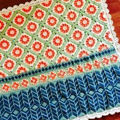 a crocheted placemat with an orange and blue design on it sitting on a wooden table