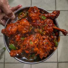 a person holding a metal bowl filled with meat and veggies on top of a tile floor