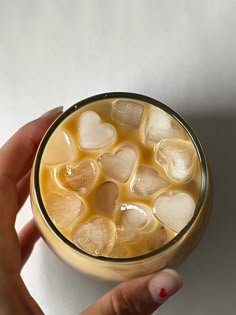 a hand holding a glass filled with liquid and ice hearts