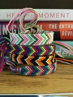 several colorful bracelets sitting on top of a wooden table next to books and a pair of scissors