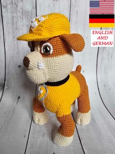 a crocheted dog wearing a yellow hat on top of a wooden floor with an american flag in the background