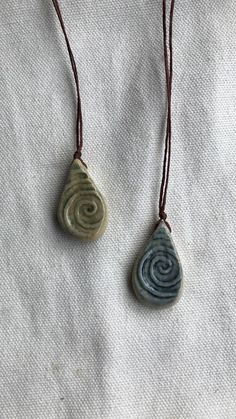 two stone pendants are on a brown cord with a white and blue swirl in the middle