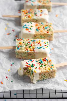 cake pops with white frosting and sprinkles lined up on a cooling rack