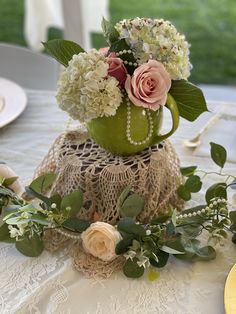 a green vase filled with flowers sitting on top of a white table covered in lace