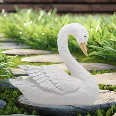 a white swan statue sitting on top of a stone walkway surrounded by green grass and plants