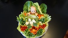 a baby doll sitting on top of lettuce and carrots