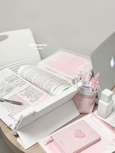 a laptop computer sitting on top of a wooden table next to papers and pens in front of it