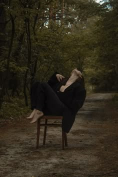 a woman laying on top of a wooden chair in the middle of a forest