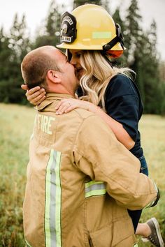 a firefighter kissing his girlfriend on the cheek in a field with trees and grass