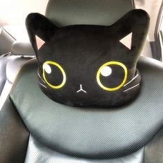 a black cat pillow sitting in the back seat of a car, with yellow eyes