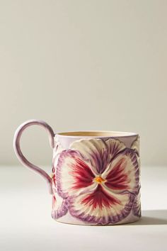 a purple and white flower mug sitting on top of a table next to a wall