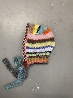 a multicolored knitted hat laying on top of a metal surface next to a string