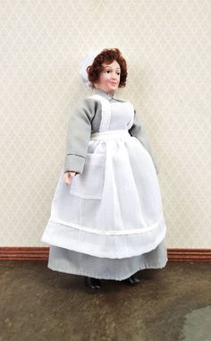 a doll is standing in front of a wall with a white dress and bonnet on it's head