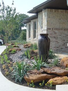 a large vase sitting in the middle of a flower bed next to a brick building