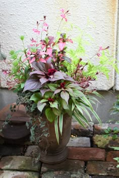 a vase filled with lots of flowers sitting on top of a brick floor next to a wall