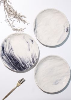 three white plates with black and white designs on them next to a silverware fork