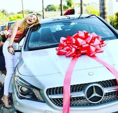 a woman standing next to a white car with a red bow on it