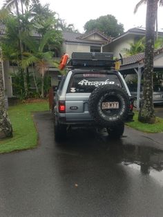 a jeep parked in front of a house on a wet road with palm trees around it