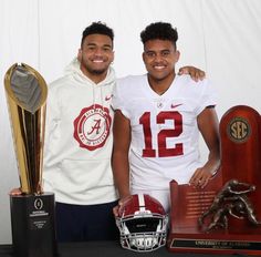 two men standing next to each other holding trophies