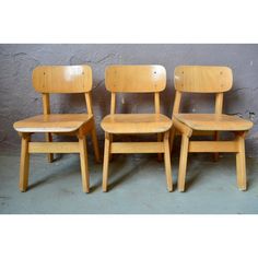 three wooden chairs sitting next to each other on a cement floor in front of a wall