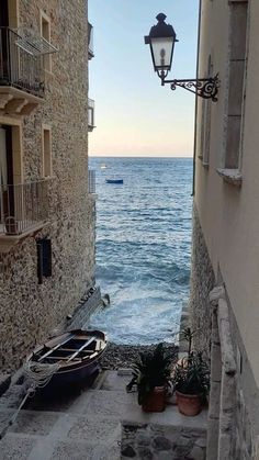 an alley way leading to the ocean with boats parked on the side and buildings in front