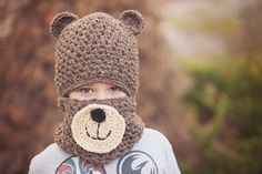 a young boy wearing a crocheted bear hat and scarf with his eyes closed