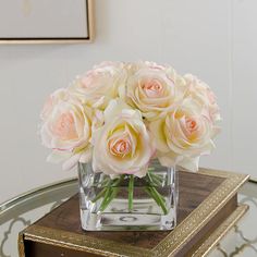 a vase filled with white and pink roses on top of a table next to a mirror