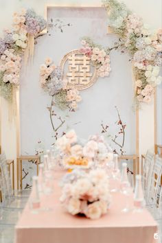 the table is set with pink and white flowers on it, along with an elaborate wall decoration