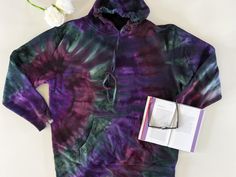 a purple and green tie - dyed hoodie with an open book next to it