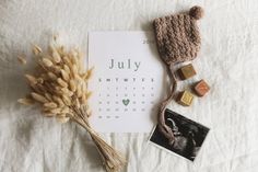 a calendar, hat, and other items laid out on a white sheet with the word july next to it