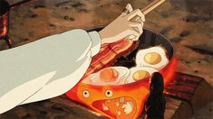 a man cooking eggs in a frying pan on an open flamed fire with chopsticks