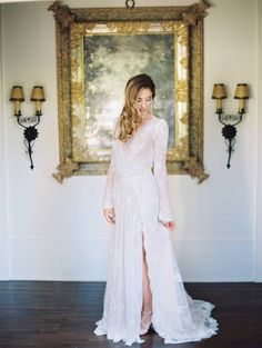 a woman standing in front of a painting wearing a long white dress with high slit