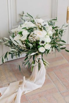 a bridal bouquet with white flowers and greenery sits on the floor in front of a door