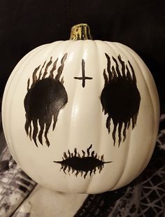 a white pumpkin decorated with black paint and a cross painted on the face is shown