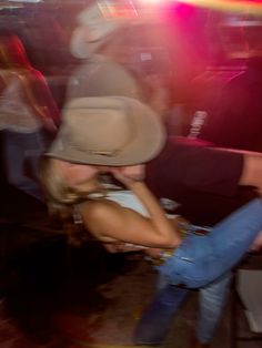 a woman wearing a cowboy hat dancing in a room with other people and lights behind her