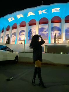 a woman standing in front of a large building with lights on it's side