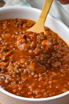 a wooden spoon in a white bowl filled with chili