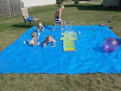 children playing in the backyard on a blue tarp with an inflatable pool