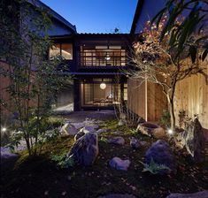 an exterior view of a house at night with lights on the windows and rocks in the foreground