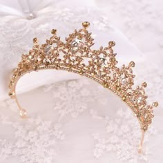 a gold tiara sitting on top of a white lace covered tablecloth next to a pillow