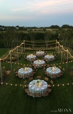 an outdoor dinner setup with string lights and tables set up in the grass at dusk